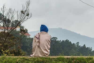 Rear view of person in shawl sitting against mountain