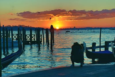 Silhouette men crouching on pier by sea against sky during sunset