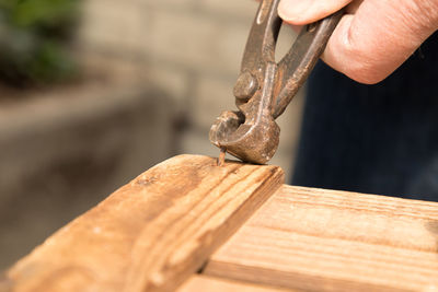 Close-up of person removing rusty nail from wood