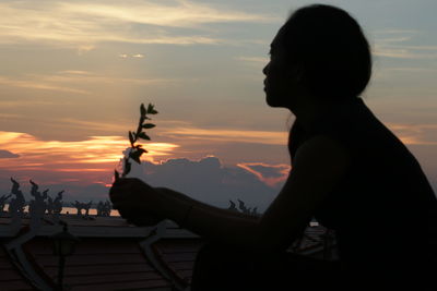 Side view of silhouette woman sitting against sky during sunset