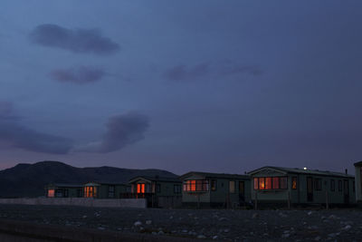 Houses by illuminated buildings against sky at dusk