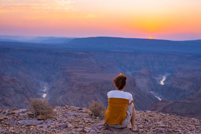 Rear view of tourist sitting on rock at namib-naukluft national park