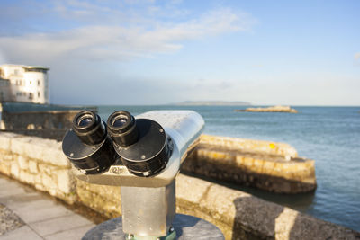 Close-up of coin-operated binoculars by sea against sky