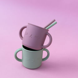 Modern pastel color silicone sippy cups with straws on pink background. baby tableware, first