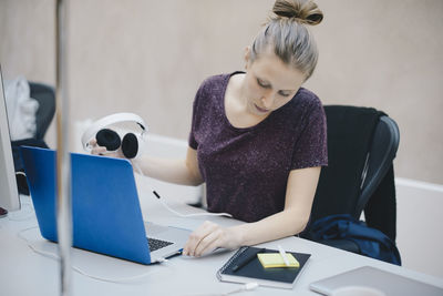 Female computer programmer connecting headphones to laptop at desk in office