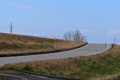 Empty road amidst field against sky