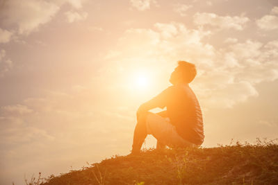 Rear view of man sitting on field against sky during sunset