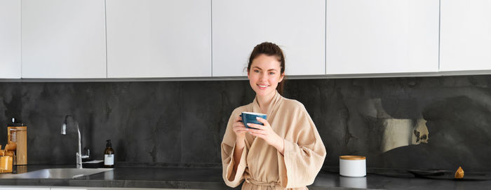 Portrait of young woman standing against wall