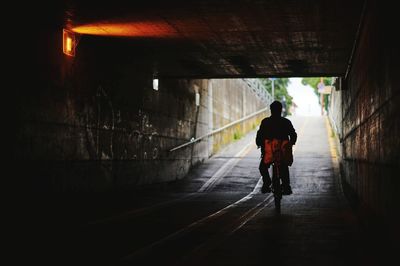 Rear view of man riding bicycle in tunnel