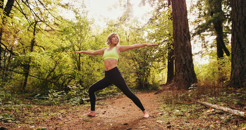 Full length of young woman with arms outstretched exercising in forest