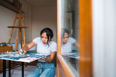 Female painter in white shirt drawing lines on easel in light studio