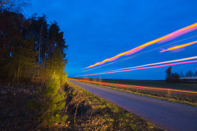 Light trails on road by trees against blue sky