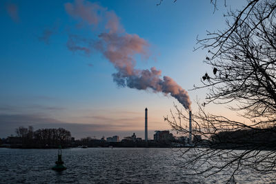 Smoke emitting from chimney by river against sky