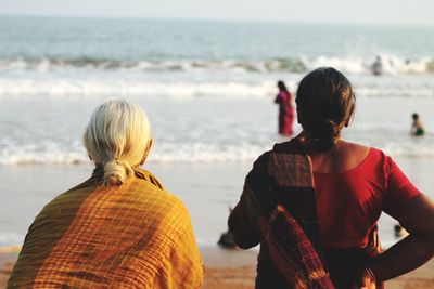 Rear view of people enjoying at beach against sky