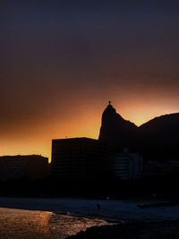 Silhouette buildings by sea against sky during sunset