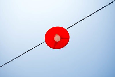 Low angle view of light bulb on cable against clear sky