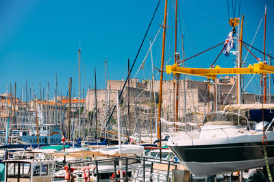 Boats moored at harbor against clear blue sky