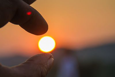 Close-up of hand holding sun during sunset