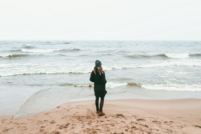 Rear view of woman walking on beach against clear sky