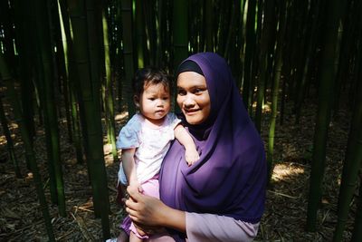 Woman carrying daughter while standing at bamboo grove