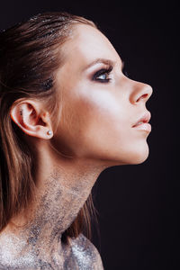 Close-up of young woman with silver body paint over black background