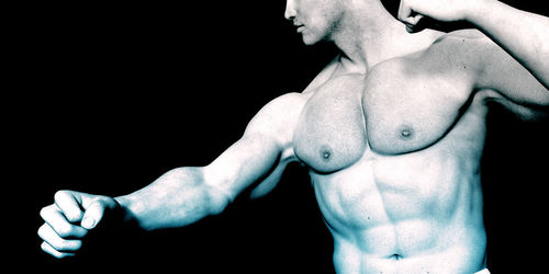 Midsection of shirtless man standing against black background