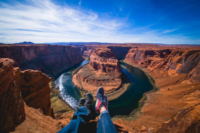 Low section of friends sitting on mountain against blue sky at grand canyon national park