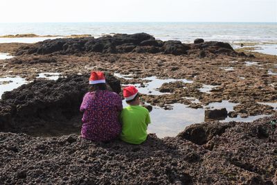 Rear view of women on rock at beach against sky