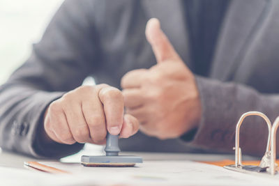 Midsection of businessman showing thumbs up while working at office