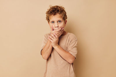 Portrait of boy gesturing against beige background