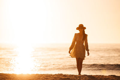 Silhouette woman standing at beach against sky during sunset