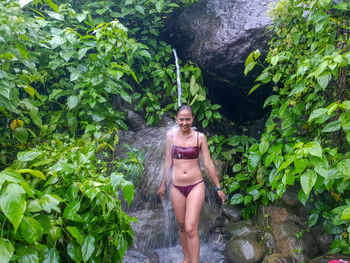 Young woman standing by plants against trees