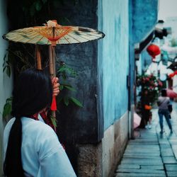 Woman with traditional umbrella standing on sidewalk in city