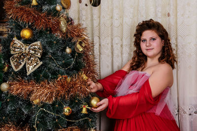 Portrait of smiling young woman standing by christmas tree