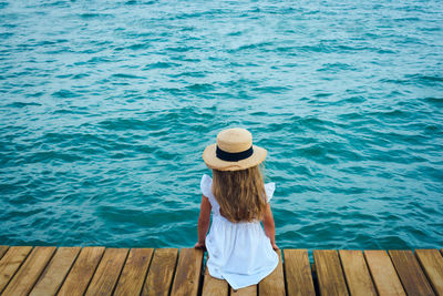 Child in straw hat on sea shore, look from behind