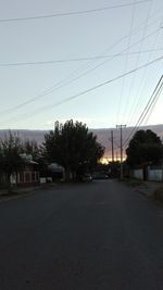 Road by trees against sky during sunset