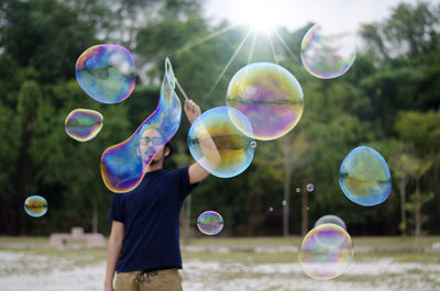 Mature man making bubbles while standing against trees
