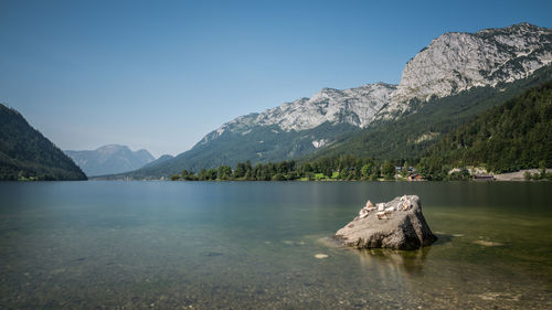 Scenic view of calm lake by mountains against clear blue sky