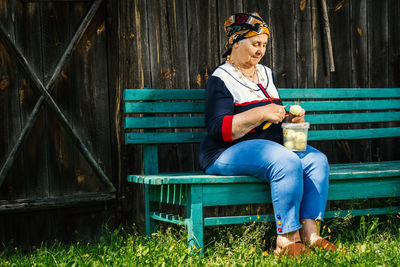 Senior woman peeling apple while sitting on bench at park