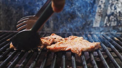 Close-up hand preparing meat on barbecue grill