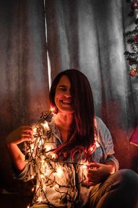 Portrait of young woman standing by christmas tree at home