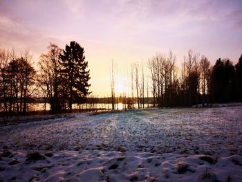 Snow covered field against sky during sunset