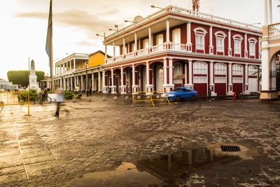 Buildings by wet street in city against sky