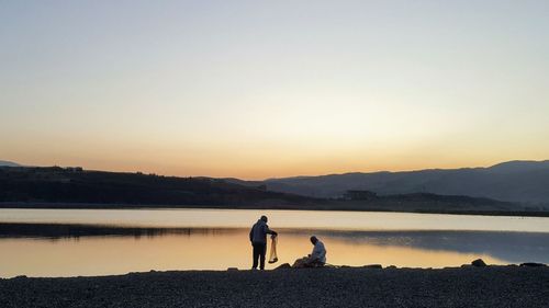 Men fishing in lake against sky during sunset