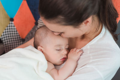 From above of cute beautiful baby in white towel sleeping on chest of crop mother at home