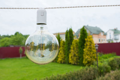 A close-up of an incandescent lamp hanging in the street in the daytime, in the garden backyard