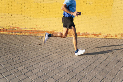 Unrecognizable senior retired man running through the city on yellow background