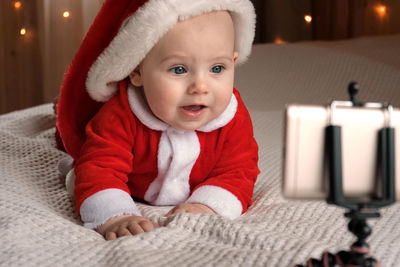 Smiling baby wearing red santa claus costume making video call looking at phone. christmas online