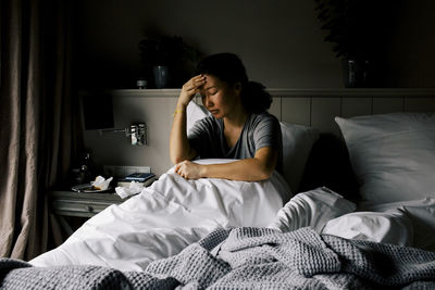 Mentally depressed woman sitting with head in hand on bed at home