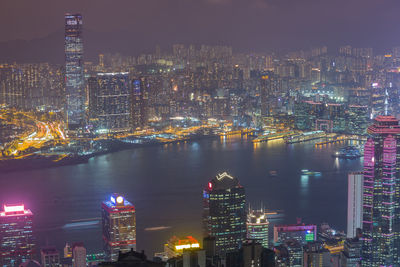 Illuminated city by river against sky at night